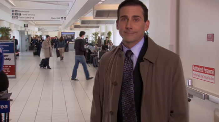 Michael Scott standing at the airport in a brown coat and tie, showcasing the best boss ever in a busy terminal setting