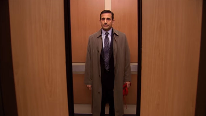 Michael Scott, the best boss ever, standing patiently in an elevator with a coat and tie, waiting for the door to close.