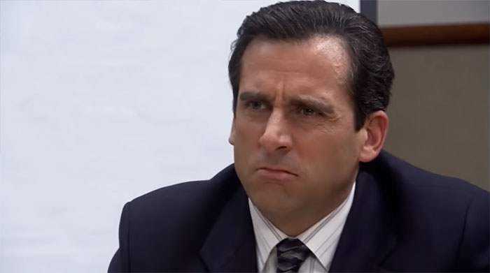 Michael Scott looking sulky, dressed in a suit and tie, expressing frustration as the best boss ever in the office.