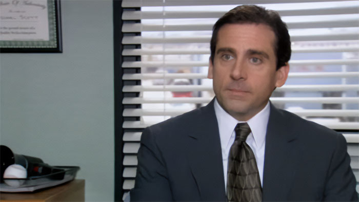 Michael Scott in a suit talking in an office setting, exemplifying quotes about the best boss ever.
