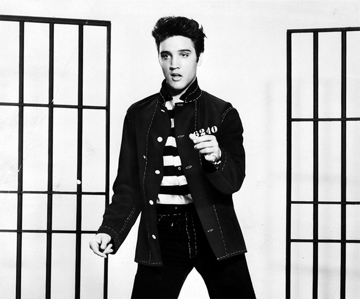 Black and white portrait of Elvis Presley in a striped shirt and jacket, an iconic figure in amazing and bizarre music facts.