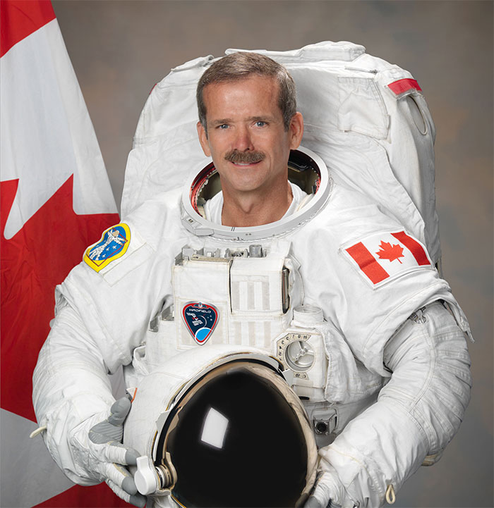 Chris Hadfield in astronaut suit holding helmet, representing amazing and bizarre music facts to soothe your ears.
