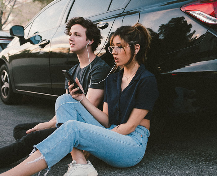 Young woman and man sitting near car, sharing earphones and enjoying music, illustrating amazing and bizarre music facts.