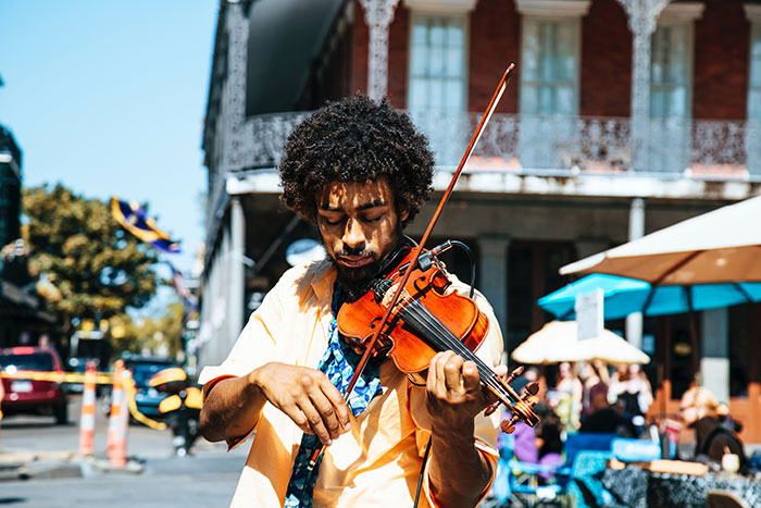 Man playing violin outdoors on a sunny day, highlighting amazing and bizarre music facts in a lively street setting