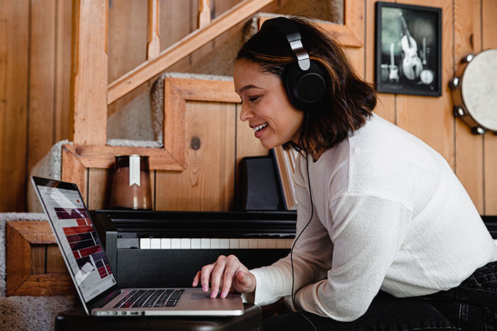Woman wearing headphones creating music on a laptop, enjoying amazing and bizarre music facts to soothe ears.