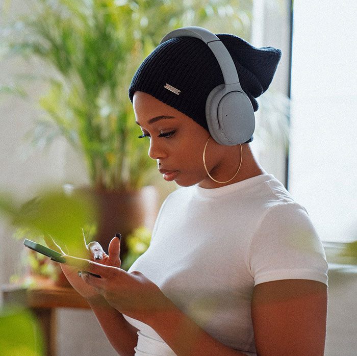 Woman wearing white shirt and headphones, focused on her device while enjoying amazing and bizarre music facts.