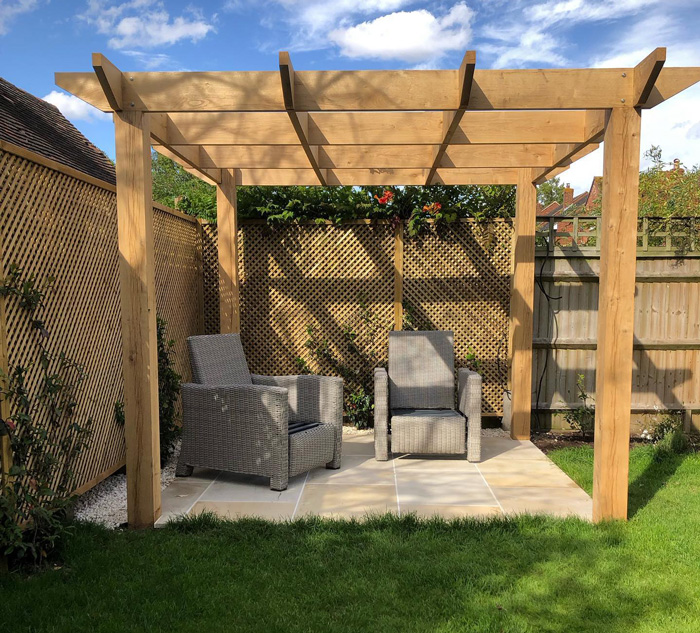 Small wooden corner pergola with seating area on patio, enhancing backyard appeal with natural wood design and greenery.
