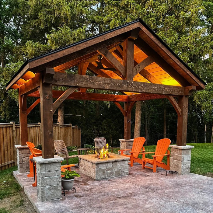 Wooden pergola with stone fireplace and orange chairs creating a stunning backyard seating area at dusk.