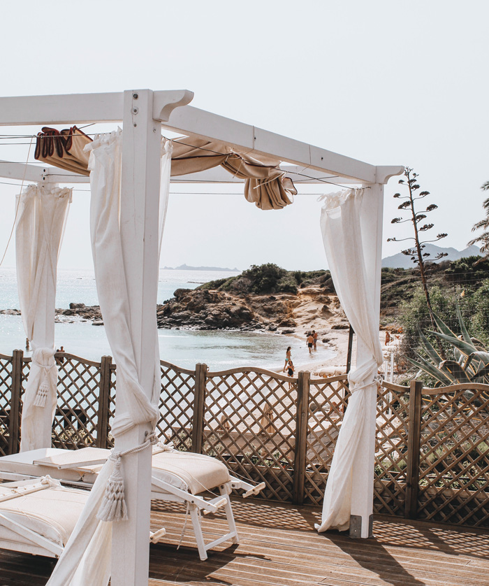 Beach pergola with flowing white curtains overlooking the rocky shoreline, enhancing backyard outdoor living ideas.