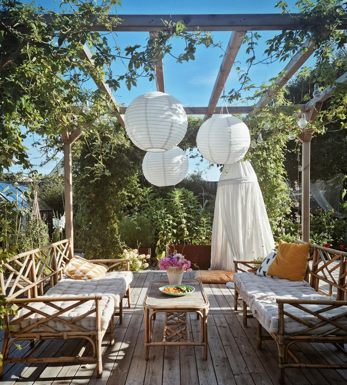 Pergola with hanging lanterns and cozy seating area surrounded by greenery for a stunning backyard look.