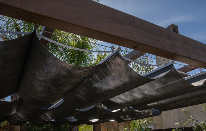 Wooden pergola canopy with fabric shade under clear blue sky, enhancing backyard pergola ideas for stunning outdoor spaces.