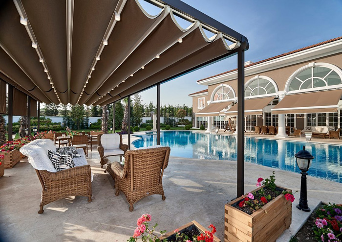 Modern pergola with rolling canopy beside a swimming pool creating a stylish and comfortable backyard retreat.