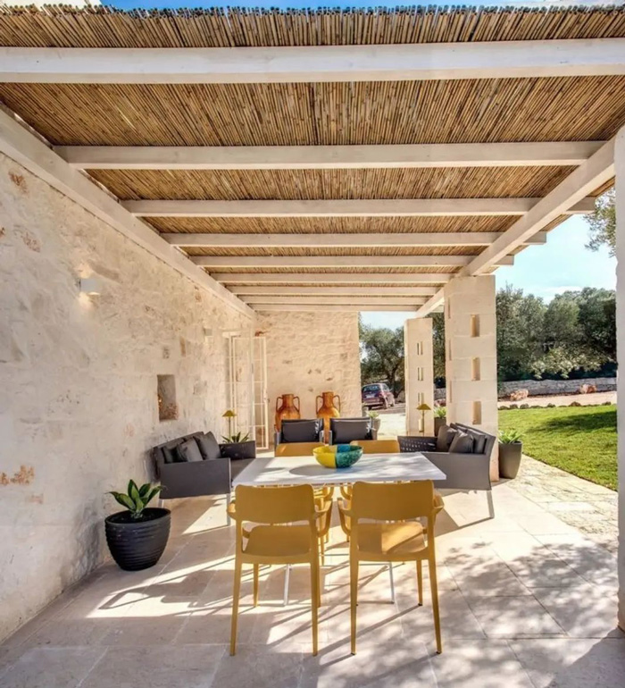 Attached straw pergola with modern outdoor seating and dining area, enhancing the backyard with stylish pergola ideas.