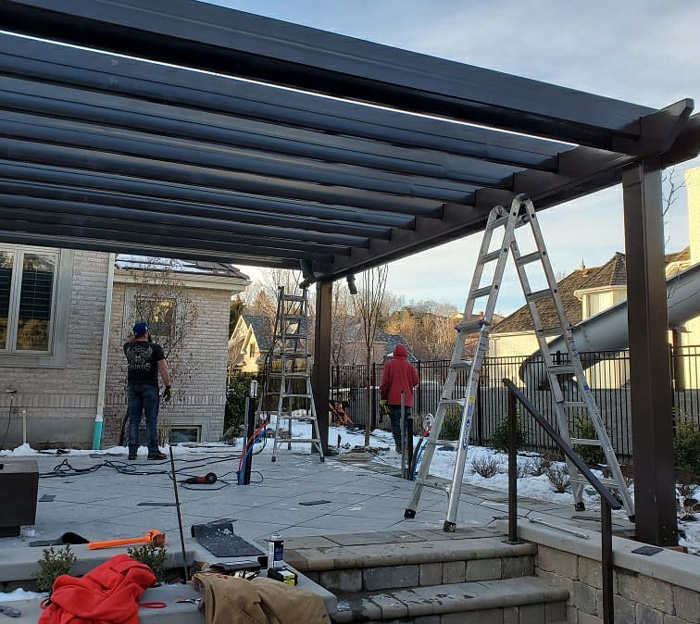 Workers assembling a modern pergola structure in a backyard, showcasing pergola ideas for outdoor living spaces.