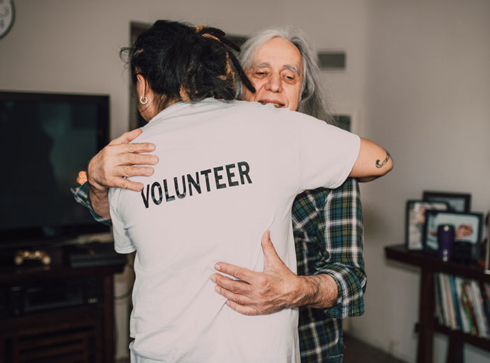 Young woman volunteering embraces older man indoors, capturing emotional family moment about fianc&eacute; and earnings reveal.