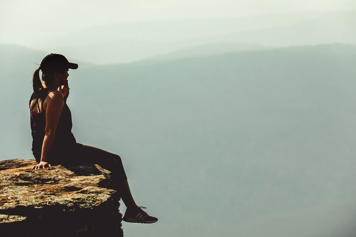 Person sitting on cliff edge deep in thought overlooking foggy mountain landscape reflecting on things said in online group