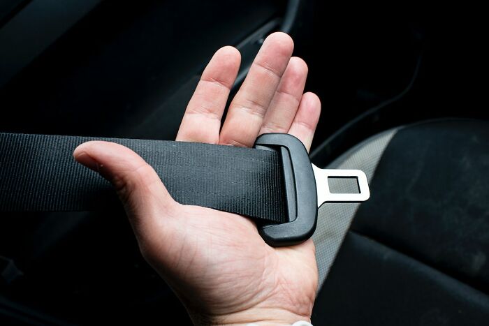 Hand holding a black car seatbelt buckle, emphasizing safety and secure fastening inside vehicle.