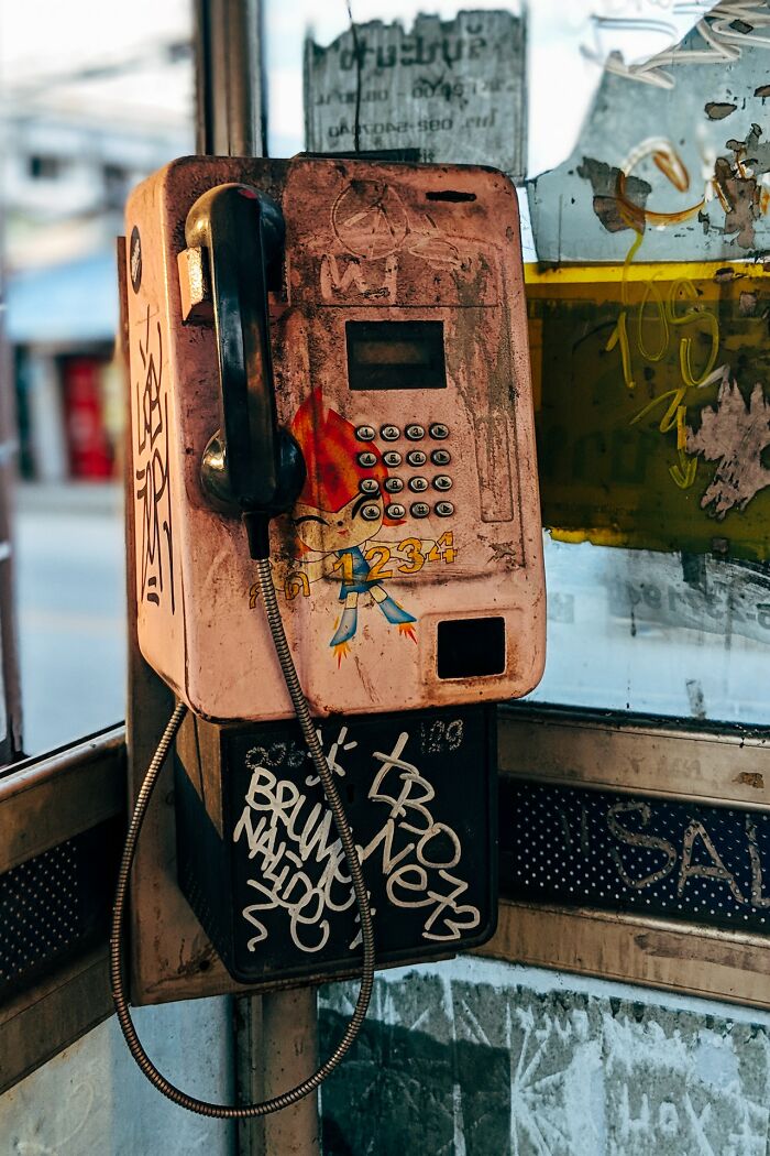Old graffiti-covered payphone in a worn booth sparking thoughts on what eventually disappeared unnoticed.