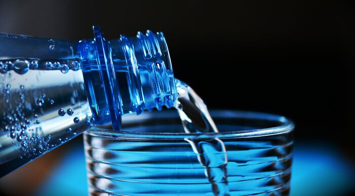 Close-up of water being poured from a blue plastic bottle into a clear glass, representing human stupidity concept visually.