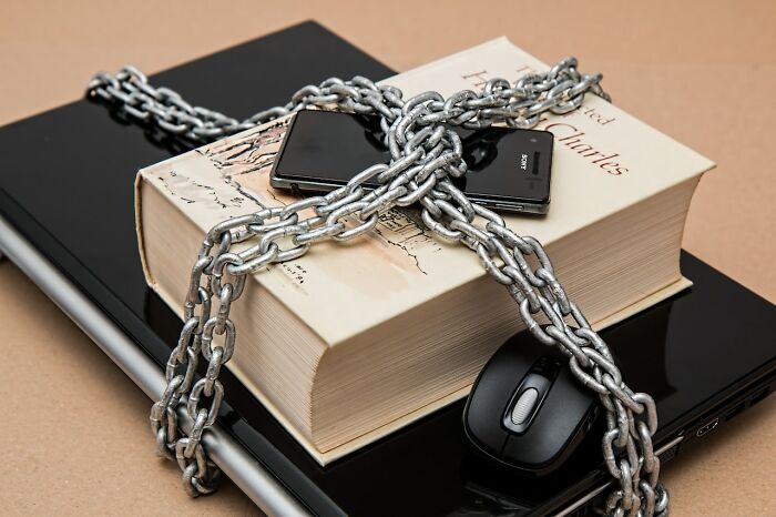 Book, smartphone, and mouse locked with chains on laptop symbolizing what eventually disappeared unnoticed.