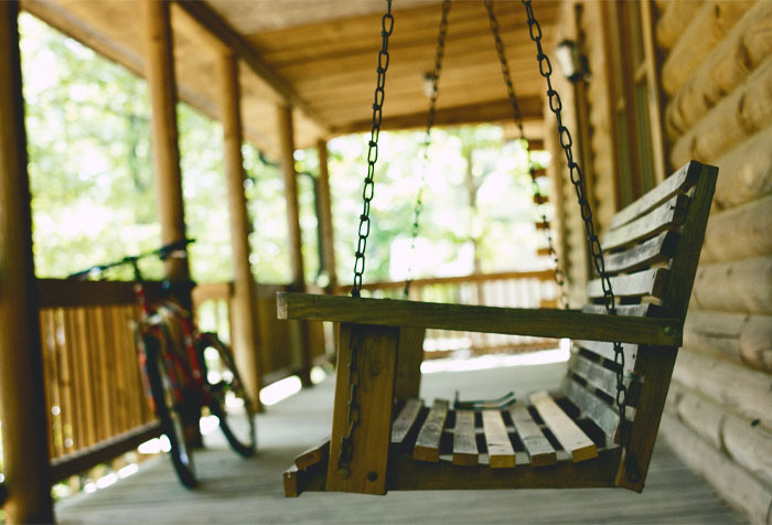 A brown wooden bench porch swing with a cycle in the background A brown wooden bench porch swing with a cycle in the background