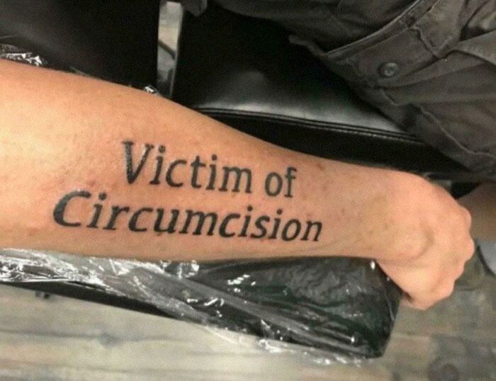 Tattoo reading "Victim of Circumcision" on a person's forearm, highlighting the importance of careful tattoo artist research.