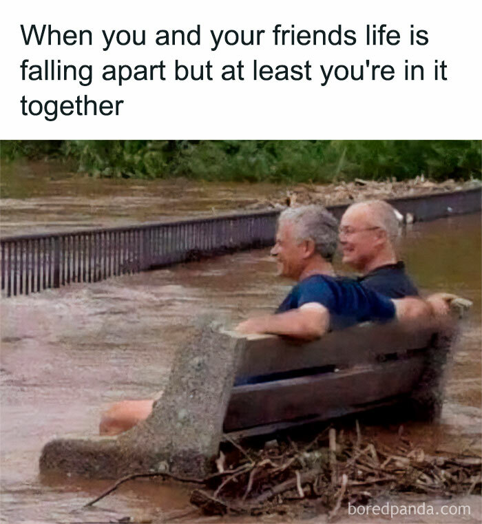 Two men sitting on a submerged bench, laughing together during a flood; a classic life meme moment.