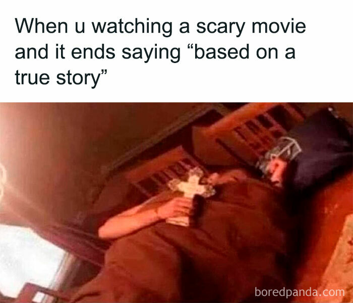 Person holding a cross in bed, reacting humorously to a true story line after a scary movie.
