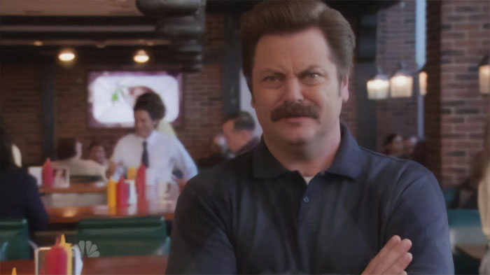 Ron Swanson looking unsatisfied with arms crossed inside a diner, embodying classic Ron Swanson quotes on life.