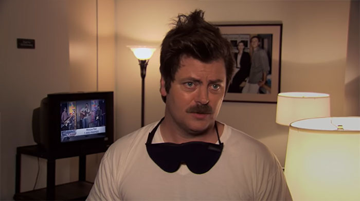 Ron Swanson wearing a sleeping mask around his neck in a warmly lit room, illustrating Ron Swanson quotes about life.