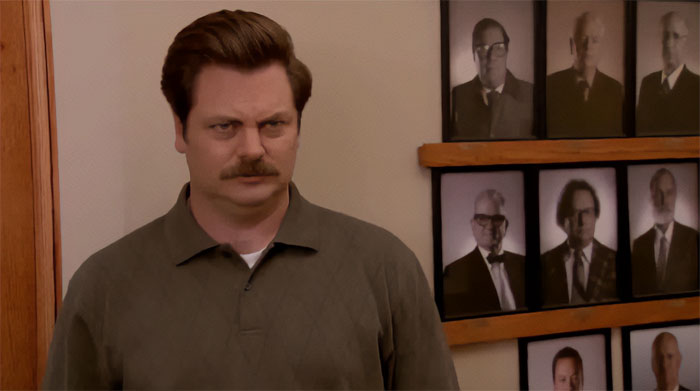 Ron Swanson looking angry, standing indoors near framed portraits, capturing a stern and intense expression for Ron Swanson quotes.