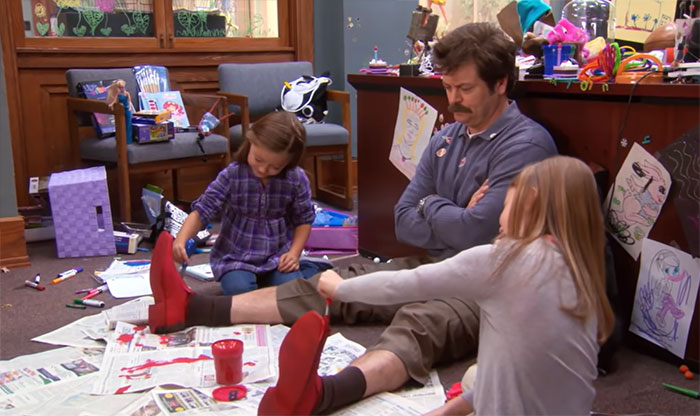 Man in casual clothes with kids coloring his red shoes, illustrating Ron Swanson quotes on life and humor.