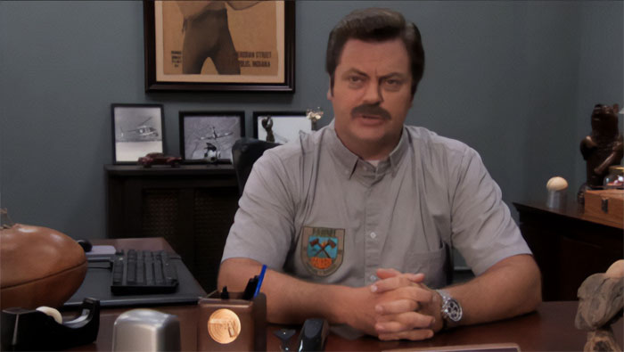 Ron Swanson sitting at his office desk, wearing a gray shirt, delivering a serious and thoughtful quote on life.