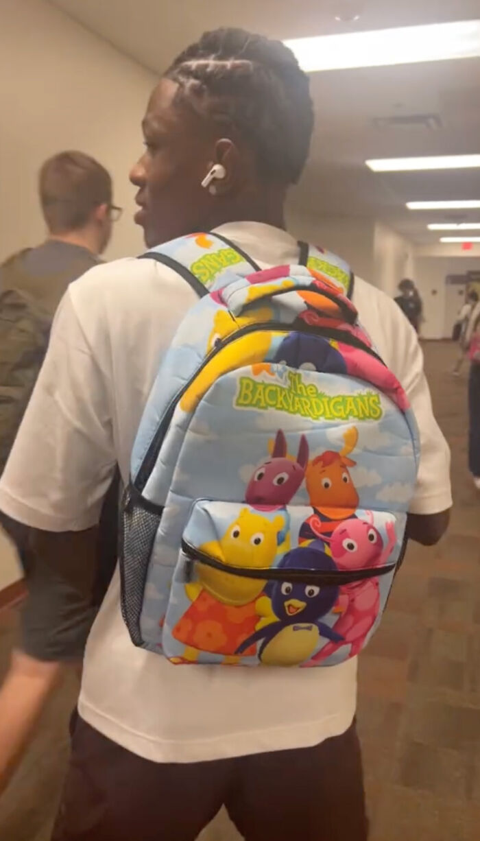 High school senior wearing a colorful kindergarten backpack with cartoon characters in a school hallway. High school senior wearing a colorful kindergarten backpack with cartoon characters in a school hallway.