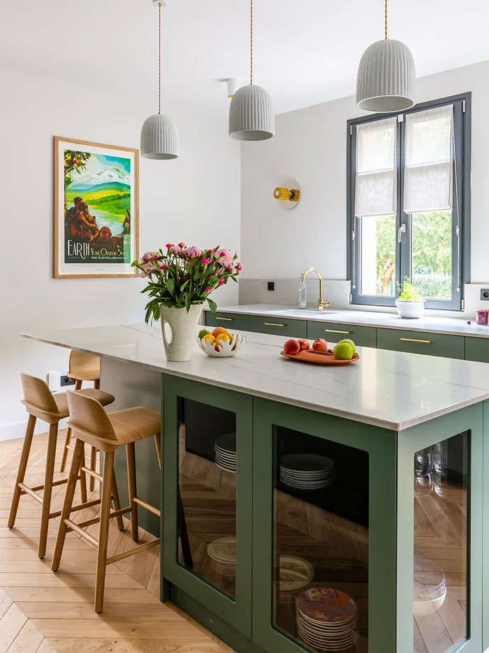 green wooden kitchen island with wooden bar chairs beside and fruits with flowers placed on it green wooden kitchen island with wooden bar chairs beside and fruits with flowers placed on it