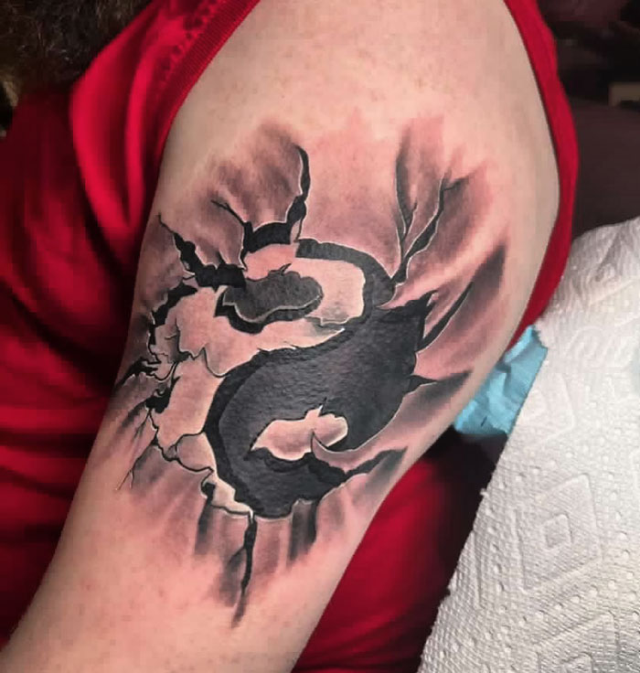 Yin Yang tattoo on upper arm with c*****d effect, symbolizing duality.