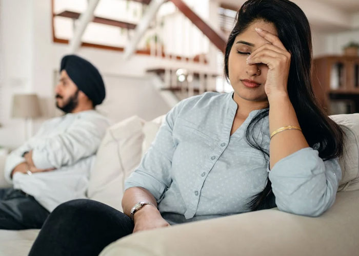 Young woman looking upset on couch while man sits in background, reflecting maid of honor breakup at wedding.