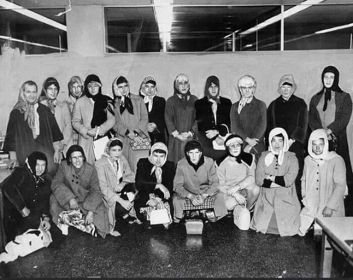 Group of women in headscarves and coats posing indoors in a black and white historical photo from the mid-20th century.