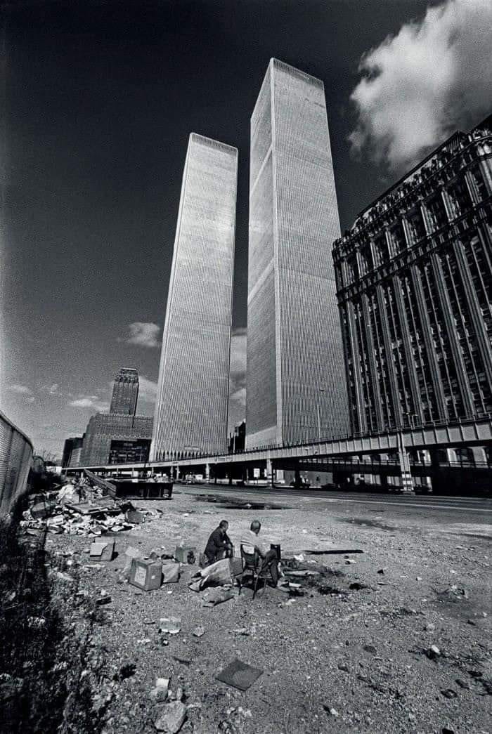 Black and white historical photo showing two people sitting near the Twin Towers under construction in New York City.