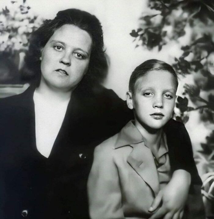 Black and white historical photo of a woman and a young boy posing together in a vintage portrait setting.