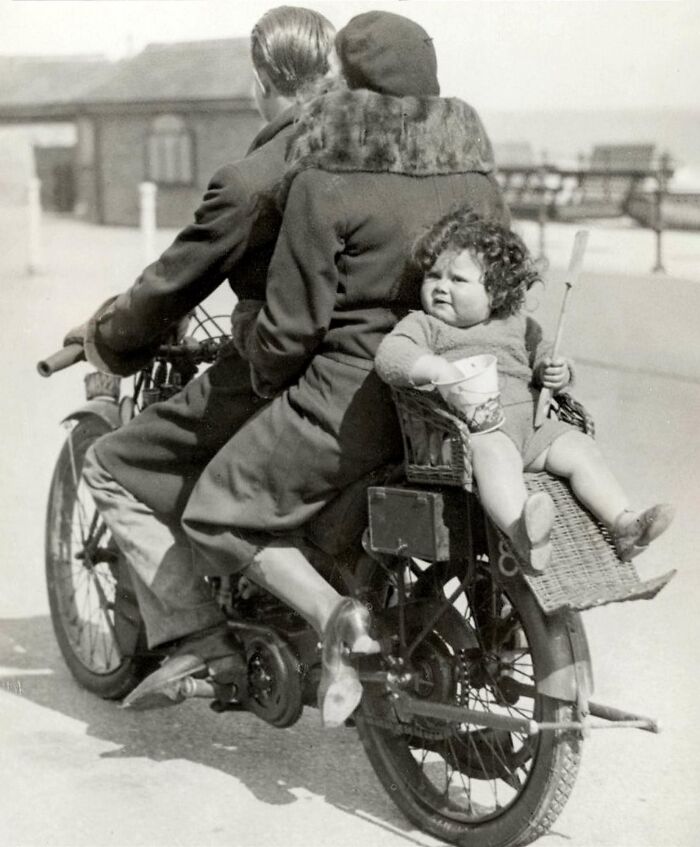 Vintage black and white photo of a family riding a motorcycle with a child in a basket, historical photos concept.