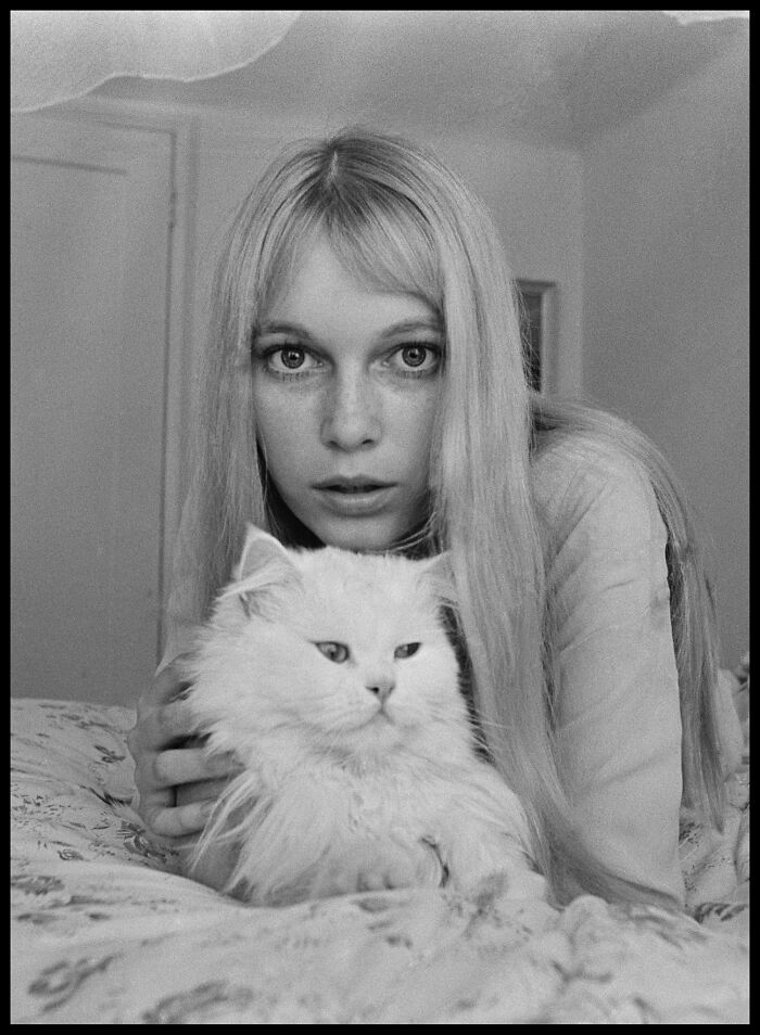 Black and white historical photo of a woman with long hair holding a fluffy white cat, looking directly at the camera.