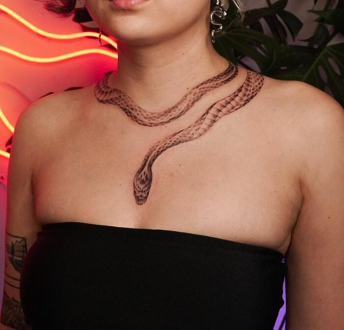 Snake tattoo encircles a woman's neck and chest, complementing her black strapless top and vibrant background.