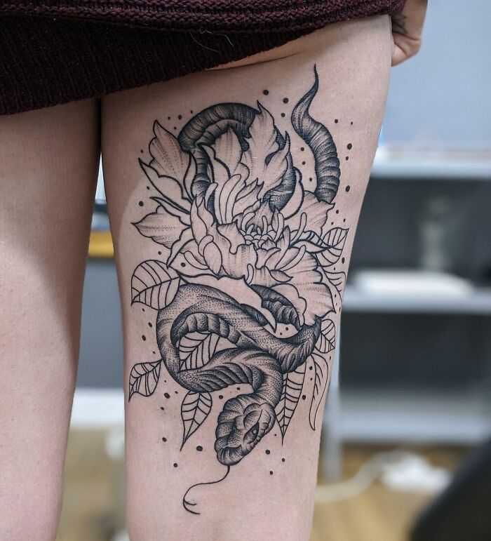 Snake tattoo on thigh entwined with floral design, showcasing intricate linework and shading.