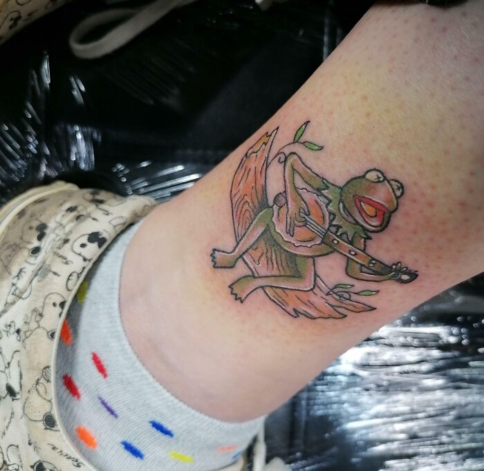 Ankle tattoo of a frog playing a banjo, designed in a whimsical style.