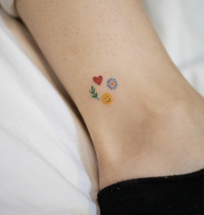 Colorful ankle tattoo featuring a heart, flower, and smiley face design for tattoo care inspiration.