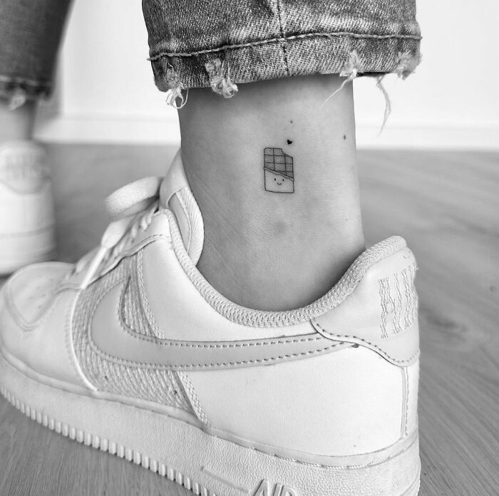 Ankle tattoo design featuring a small geometric shape, paired with white sneakers and distressed jeans.