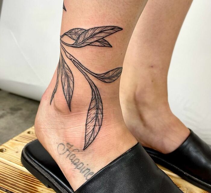 Ornate leaf ankle tattoo on a leg wearing black slippers, highlighting tattoo care and design inspiration.