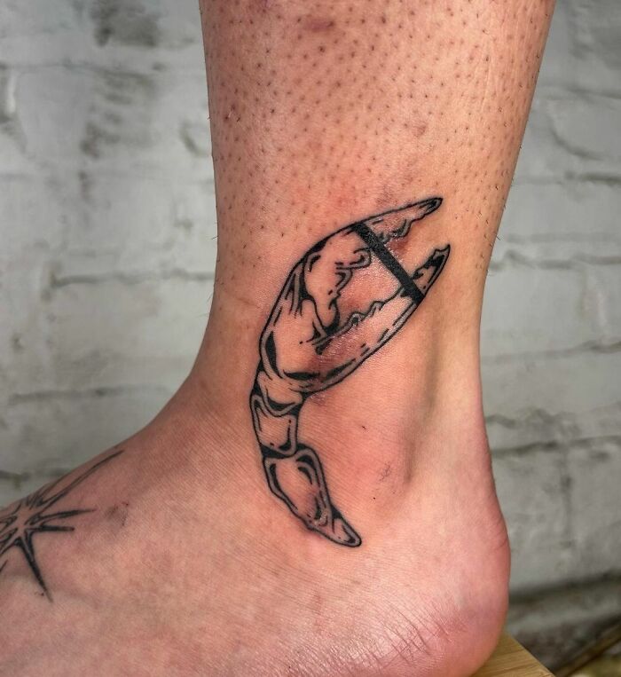 Ankle tattoo of a crab claw in black ink, showcasing unique design inspiration.