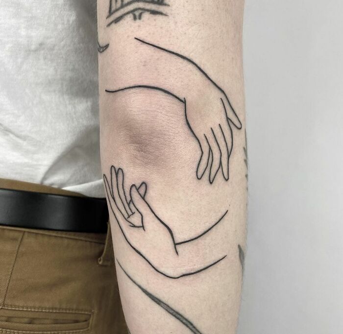 Minimalist line art elbow tattoo featuring intertwined hands.